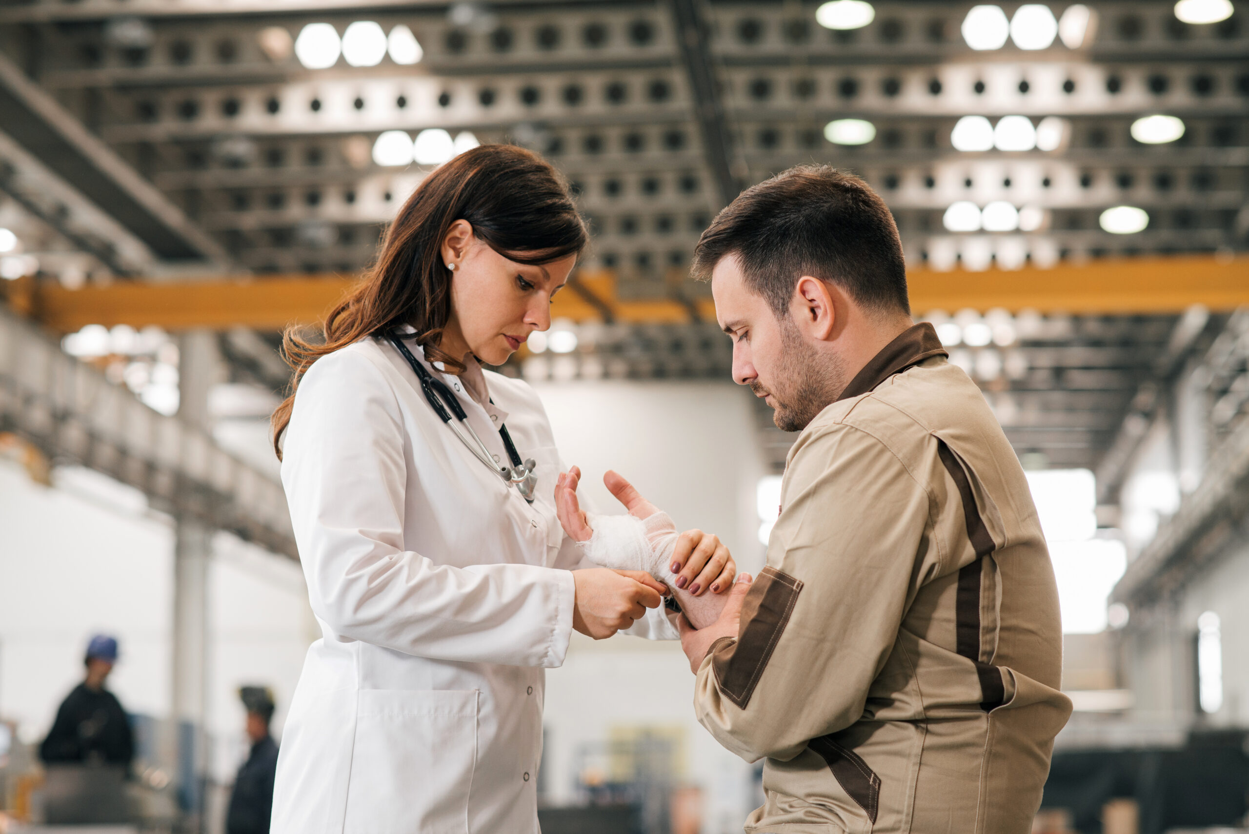 Doctor helping manual worker with an arm injury at the metal industry factory.